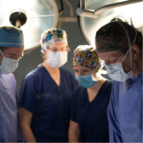 A group of doctors and nurses in scrubs and masks working in an operating room at a hospital.